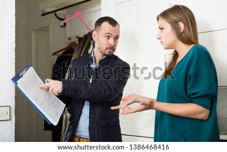 Portrait of young frustrated woman talking to debt collector visiting her at home and demanding to pay debts