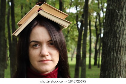 Portrait of a young and funny brunette in the park holding an open book on her head. Learning is fun. Woman balancing with books on her head. The student is tired of reading.