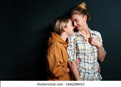 Portrait of young gay couple, lesbian women hugging on black background with copy space. Сoncept of love, family, gay marriage and pride