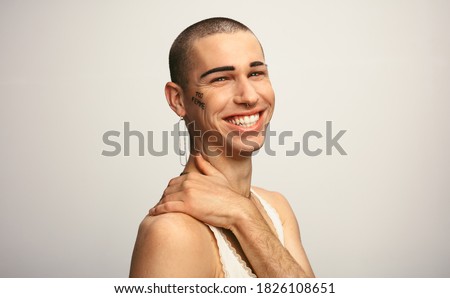 Portrait of a young gay man wearing earring looking happy on white background. Gender fluid man smiling on white background.
