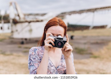 Portrait of a young ginger caucasian girl with freckles taking photos outdoors. Gorgeous woman phtographer posind with camera in summer