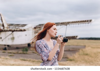 Portrait of a young ginger caucasian girl with freckles taking photos outdoors. Gorgeous woman phtographer posind with camera in summer