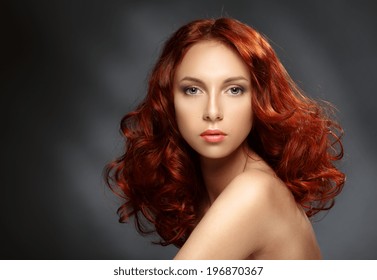 Portrait Of A Young Ginger Woman On A Dark Background. Low Key. Long Curly Red Hair. 