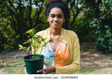 portrait young girl with afro standing looking at the camera in the field holding a plant in a pot to transplant to the earth, girl who is going to plant a Paraguayan lily.