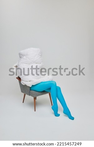 Portrait of young girl in blue tights sitting on chair covered with blanket isolated on grey studio background. Hiding from reality. Concept of retro fashion, art photography, style, queer, beauty, ad