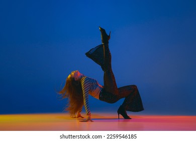 Portrait of young girl dancing, training heels dance in stylish clothes over blue background in neon light. Concept of dance lifestyle, modern style, contemporary, youth culture, self-expression