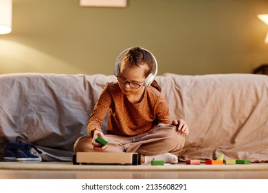 Portrait of young girl with down syndrome playing with toy blocks alone and wearing noise cancelling earphones, overstimulation concept, copy space