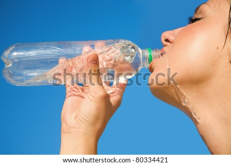 Portrait of young girl, drinking a water on background of blue sky.