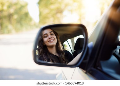 Portrait of a young girl driver through the rearview mirror of a modern car in a highway in the evening