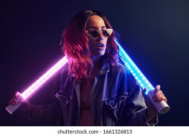 Portrait Of Young Girl In Glasses Holding Light Sticks In Red And Blue Neon In Studio.