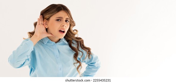 Portrait of a young girl with hand on ear. What did you say? Isolated on white background - Shutterstock ID 2255435231