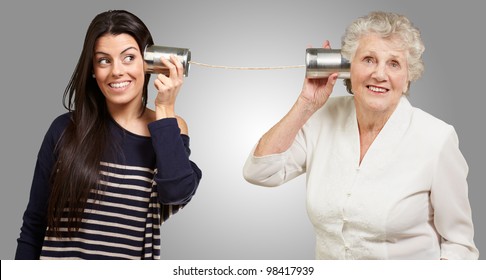 portrait of a young girl and her grandmother hearing sounds using a metal tin can over a grey background