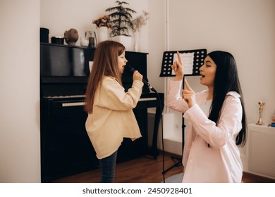 Portrait of a young girl and her mother practicing singing song during a piano lesson at home. Little female kid studying plng piano at school. - Powered by Shutterstock