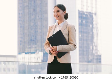 Portrait young girl lawyer student in suit hold clipboard with files and smile on city street. Beautiful happy business woman with documents folder in hands outdoors. Successful female entrepreneur