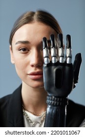 Portrait Of Young Girl Looking At Camera Through Prosthetic Arm Isolated On Blue Background