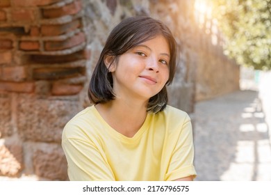 Portrait of a young girl on the background of a stone wall with an arch. A girl with dark hair poses for the camera.