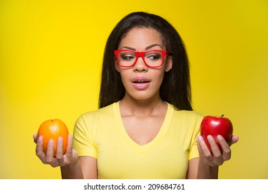 Portrait Of Young Girl standing on yellow background. beautiful woman holding red apple and orange  