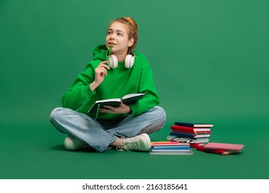 Portrait of young girl, student in casual cloth sitting on floor with thoughtful expression, studying isolated over green studio background. Concept of education, studying, homework, youth, lifestyle - Shutterstock ID 2163185641