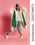 Portrait of young girl in sunglasses, blue hat, green scarf and fur coat posing over pink background. Stylish youth. Concept of beauty, winter fashion, lifestyle, emotions, facial expression. Ad