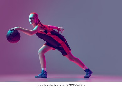 Portrait Of Young Girl, Teen, Basketball Player In Motion Dribbling Ball, Training Isolated On Gradient Pink Purple Background In Neon. Concept Of Professional Sport, Health, Active Lifestyle, Hobby