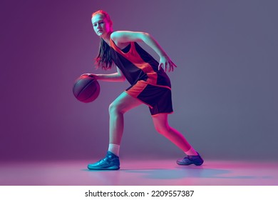 Portrait Of Young Girl, Teen, Basketball Player In Motion, Training Isolated On Gradient Pink Purple Background In Neon. Dribbling Ball. Concept Of Professional Sport, Health, Active Lifestyle, Hobby