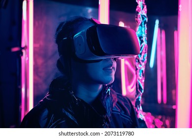 Portrait Of Young Girl Wearing Virtual Reality Goggles. She Is Surrounded With Neon Light. Virtual Reality Point Of View Concept