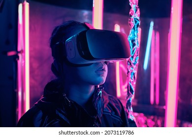 Portrait Of Young Girl Wearing Virtual Reality Goggles. She Is Surrounded With Neon Light. Virtual Reality Point Of View Concept