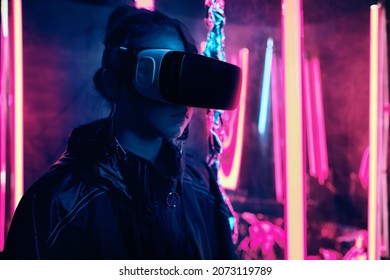 Portrait Of Young Girl Wearing Virtual Reality Goggles. She Is Surrounded With Neon Light. Virtual Reality Point Of View Concept