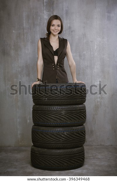 Portrait of a young girl who is\
inside automobile tires, on the background of gray concrete\
wall.