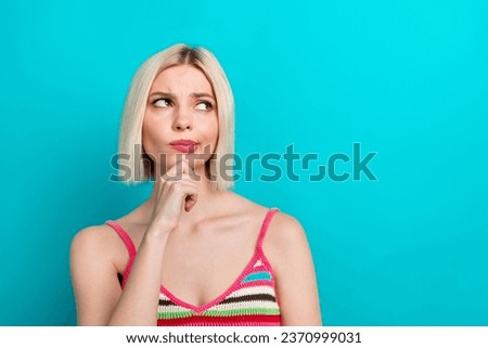 Portrait of young girlfriend wearing knitted striped stylish singlet touch chin looking empty space isolated on aquamarine color background