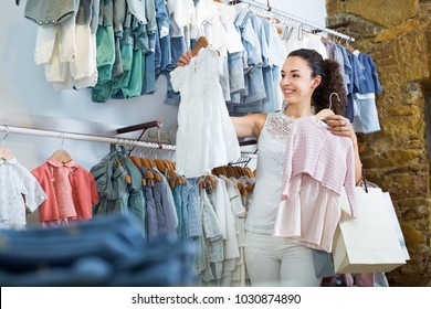 Portrait Of Young Glad Woman Shopping Baby Dress At The Kids Clothes Store 