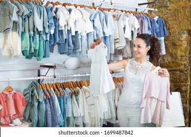 Portrait Of Young Glad Woman Shopping Baby Dress At A Kids Clothes Store 