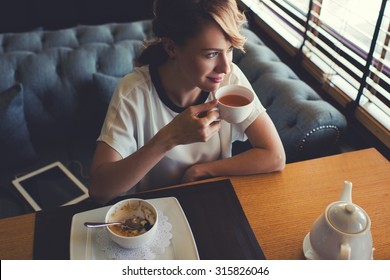 Portrait of young gorgeous female drinking tea and looking with smile out of the coffee shop window while enjoying her leisure time, nice business woman lunch in modern cafe during her work break - Powered by Shutterstock