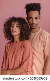 Portrait Young Group People Of Exotic Appearance Different Sex On Isolated Pink Background. Beautiful Woman With Lush Curly Hair Stands With Her Back To Serious Man With Beautifully Shaved Beard.