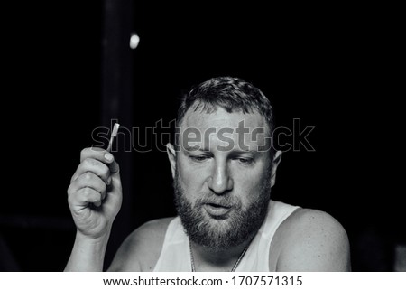 portrait of young grumpy bearded red hair man with sigaret horizontal. A man with a red beard smokes. The guy smokes an electronic cigarette. A man in a white T-shirt. Relaxation. Evening photo