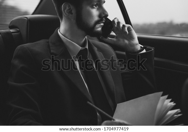 portrait of a young guy thirty years old.\
Businessman in a business style of clothing. Rides in the passenger\
seat at the office to work, solving problems on the smartphone,\
talking on the phone
