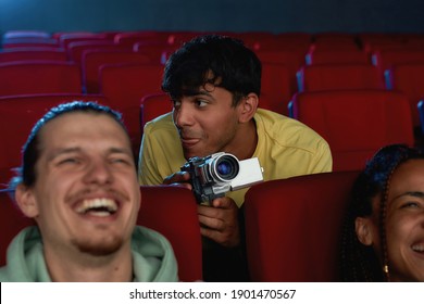 Portrait of young guy using his video camera for recording a pirated movie at the cinema. Selective focus. Horizontal shot