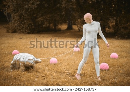 Portrait of young hairless girl with alopecia in white cloth walking tardigrade toy in fall park, surreal scene with bald teenage girl reflect on intertwining threads of life and art