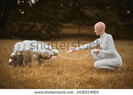 Portrait of young hairless girl with alopecia in white cloth playing with tardigrade toy in fall park, surreal scene with bald teenage girl reflect on intertwining threads of life and art