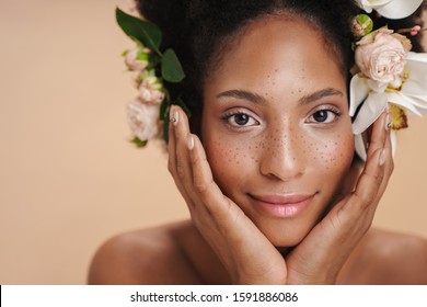 Portrait of young half-naked freckled african american woman with flowers in her hair isolated over beige background