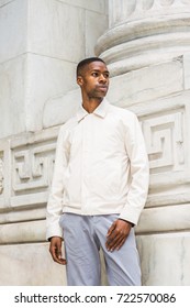 Portrait of Young Handsome African American Man in New York. Young black man wearing light color jacket, standing by vintage marble wall, looking, thinking, lost in thought.