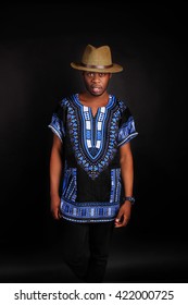 portrait of young handsome african man wearing bright blue national costume smiling gesturing. Stylish young black man in traditional clothes posing on dark background.