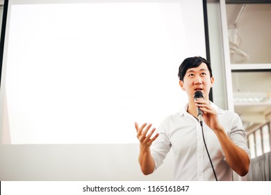 Portrait Of Young Handsome Asian Male Speaker Publicly Speaking On Stage To Group Of Audience With White Board Behind