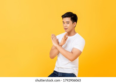 Portrait of young handsome Asian man showing disagreement by doing x crossed hand gesture in isolated studio yellow background