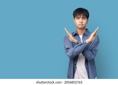 Portrait Of Young Handsome Asian Man Showing STOP Or Rejection Expression Crossing Arms Doing Negative Sign, Angry Face, Isolated Blue Color Background.