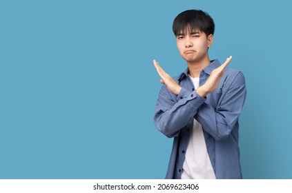 Portrait Of Young Handsome Asian Man Showing STOP Or Rejection Expression Crossing Arms Doing Negative Sign, Angry Face, Isolated Blue Color Background.