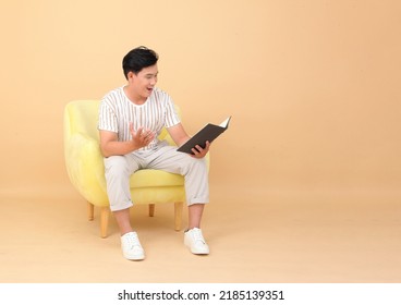 Portrait Of A Young Handsome Asian Office Man Sitting On Sofa Chair And Reading Book, Concept Of New Normal Life Or Work From Home As A Freelancer, Isolated On Background