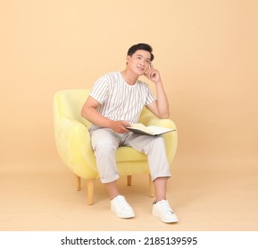 Portrait Of A Young Handsome Asian Office Man Sitting On Sofa Chair And Reading Book, Concept Of New Normal Life Or Work From Home As A Freelancer, Isolated On Background