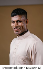 Portrait Of A Young, Handsome And Athletic Malaysian Indian Muslim Man In A Cream Colored Traditional Baju Melayu Tunic. He Is Dressed Festively To Go Visiting For Raya. He Is Smiling Happily. 