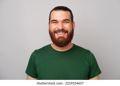 Portrait Of Young Handsome Bearded Man Wearing Green T-shirt And Smiling At The Camera Over Grey Backdrop.